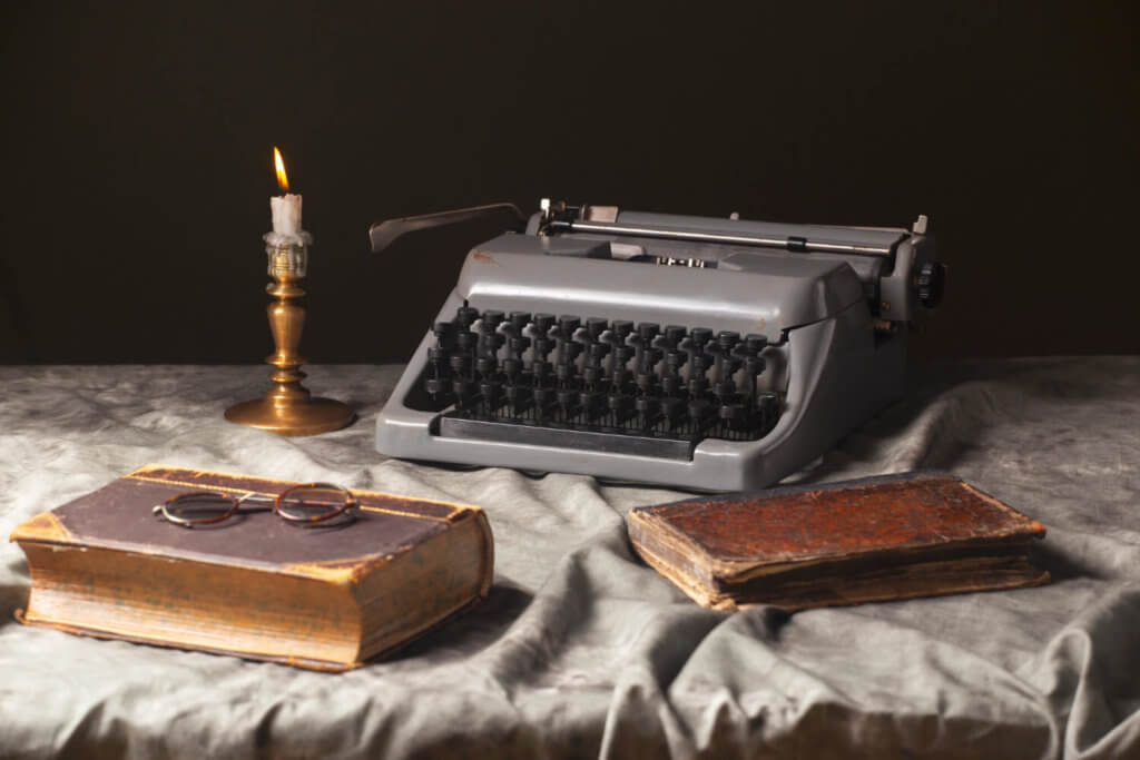 A table with a typewriter, lit candle and old books on top