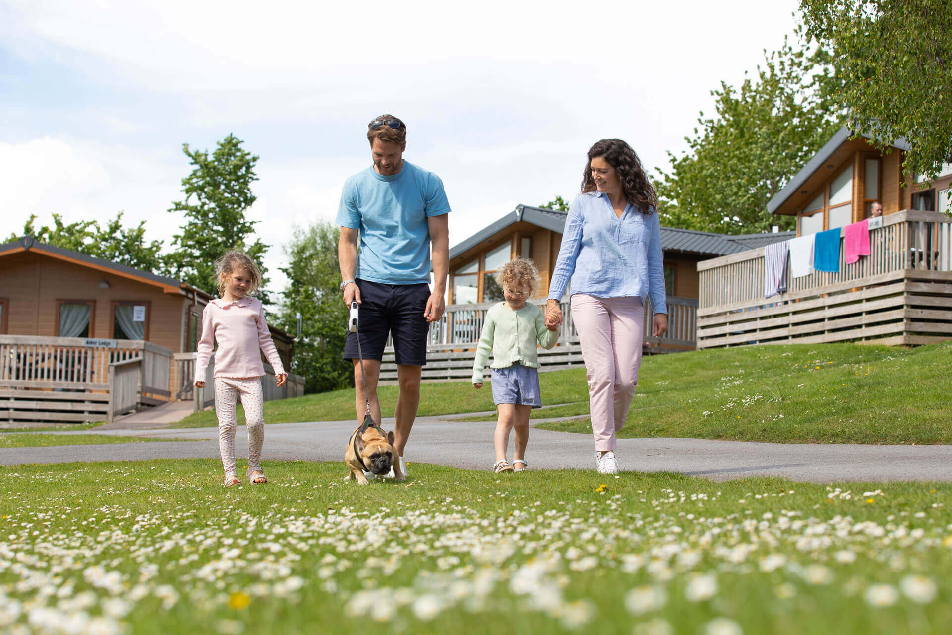 Smiling family walking their dog through a field with lodges in the background