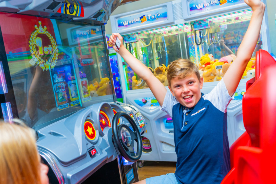 Boy celebrating after winning a driving game at an arcade on his Devon break