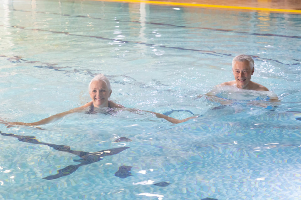 Two elderly people swimming in an indoor pool